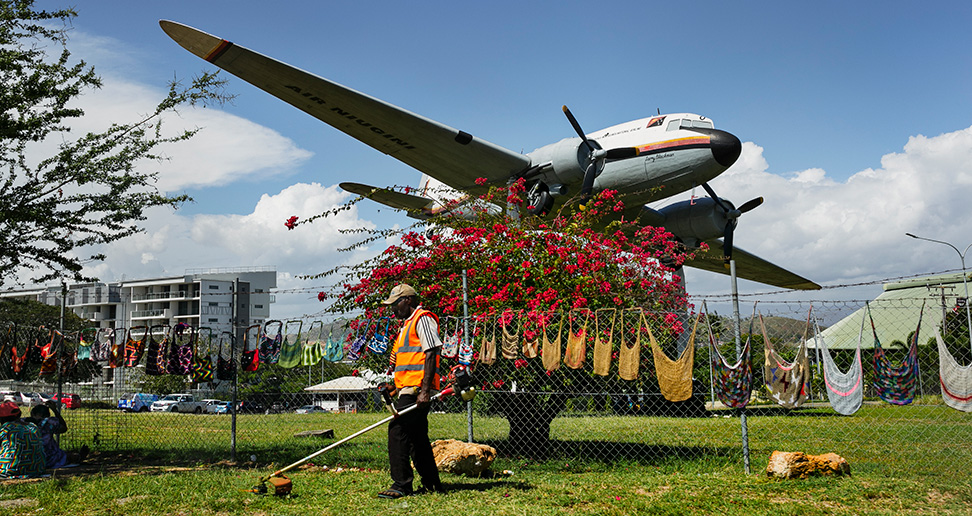 A man picking up rubbish in front of an old plane in a field — © Stephen Dupont